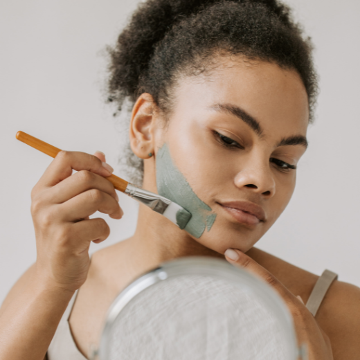 Woman applying skin care mask to her face with a mask applicator brush while looking in the mirror