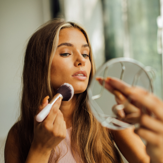 Woman Applying Skin Healthy Makeup Using A Makeup Brush and Mirror